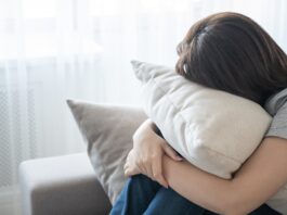 Woman sitting on couch and hugging a pillow, loneliness and sadness concept